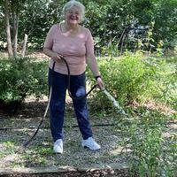 Cindy stands with a hose watering some shrubs