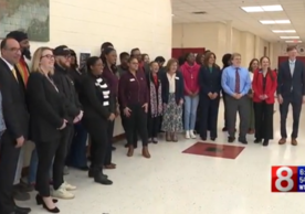 25 city leaders stand in the hallway of Wilbur Cross High School.