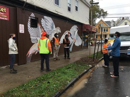 Kwadwo Adae and GreenSkills planting crew in front of mural and tree
